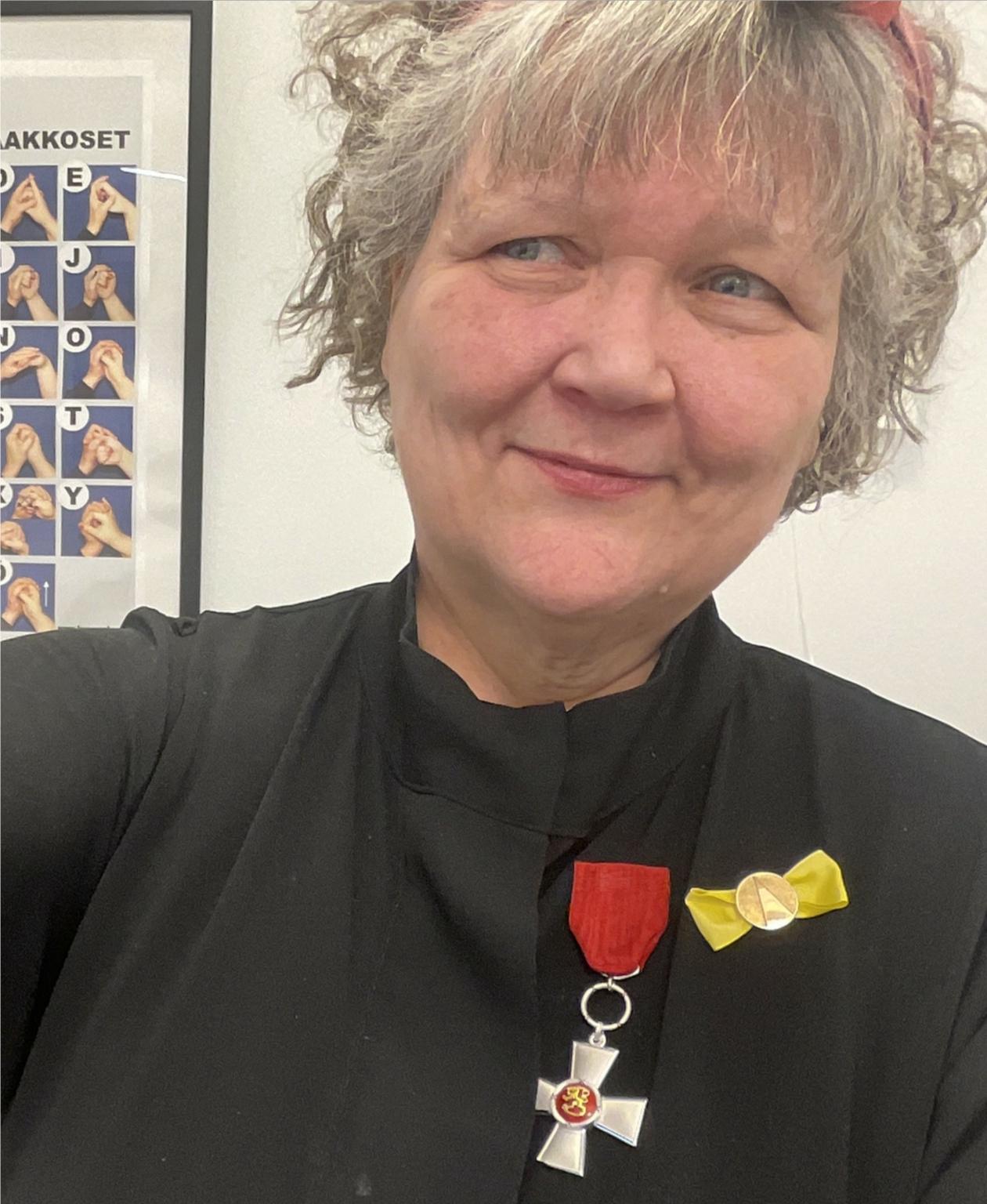 Hymyileva nainen tummassa juhlapuvussa, jonka rintamukseen on kiinnitetty Suomen Leijonan ansioristi ja Näkövammaisten liiton kultainen ansiomerkki